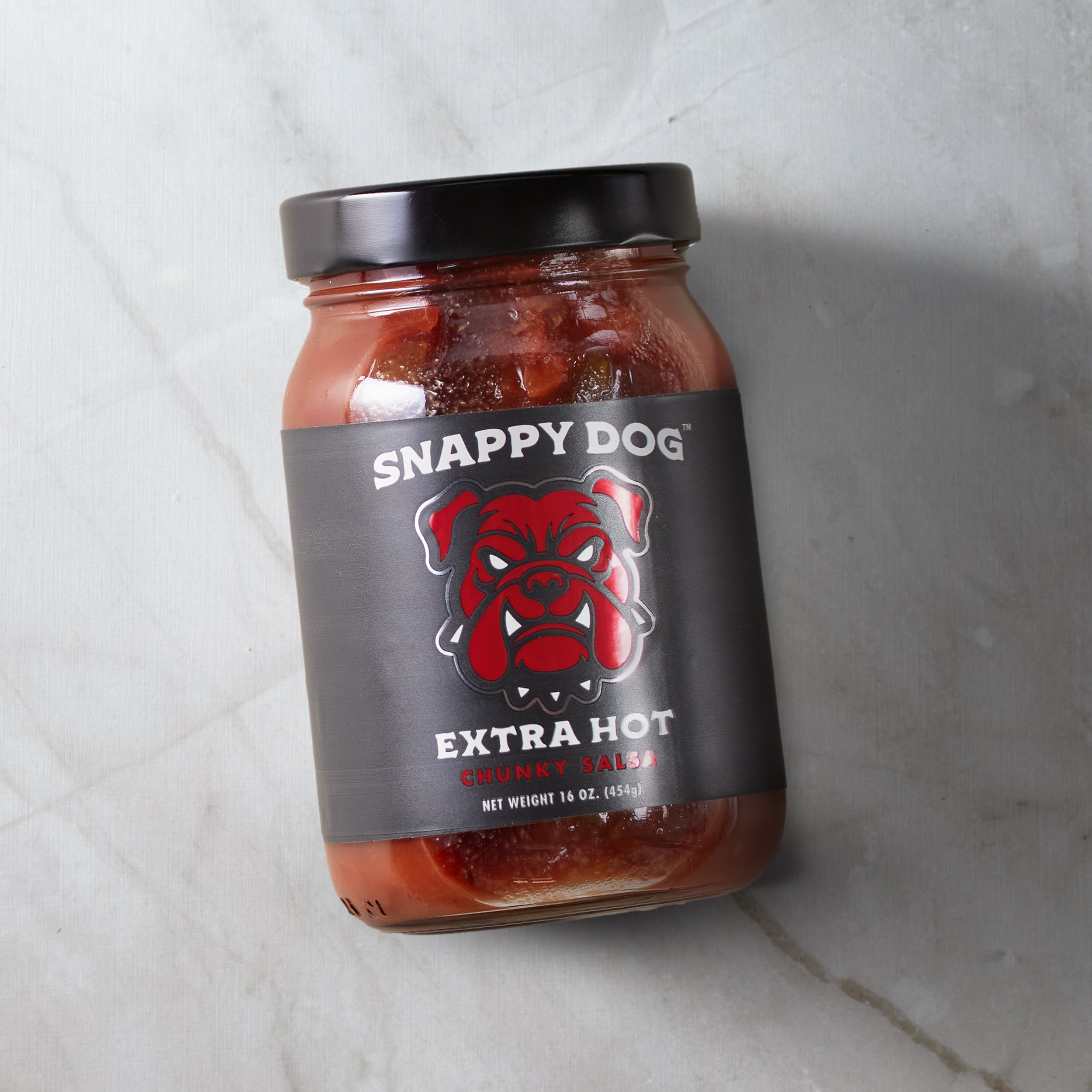 Jar of Snappy Dog Extra Hot chunky salsa, with black label, that has metallic red dog head of snappy dog logo.